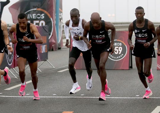 In this Oct. 12, 2019 photo, marathon runner Eliud Kipchoge from Kenya, white vest, wearing Nike AlphaFly prototype running shoe, and his first pacemaking team, wearing pink Nike Vaporfly shoes, leave the start line in an attempt to run a sub two-hour marathon in Vienna, Austria. (AP Photo/Ronald Zak, File)