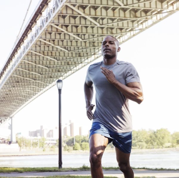 Sportsman running on field against bridge in city