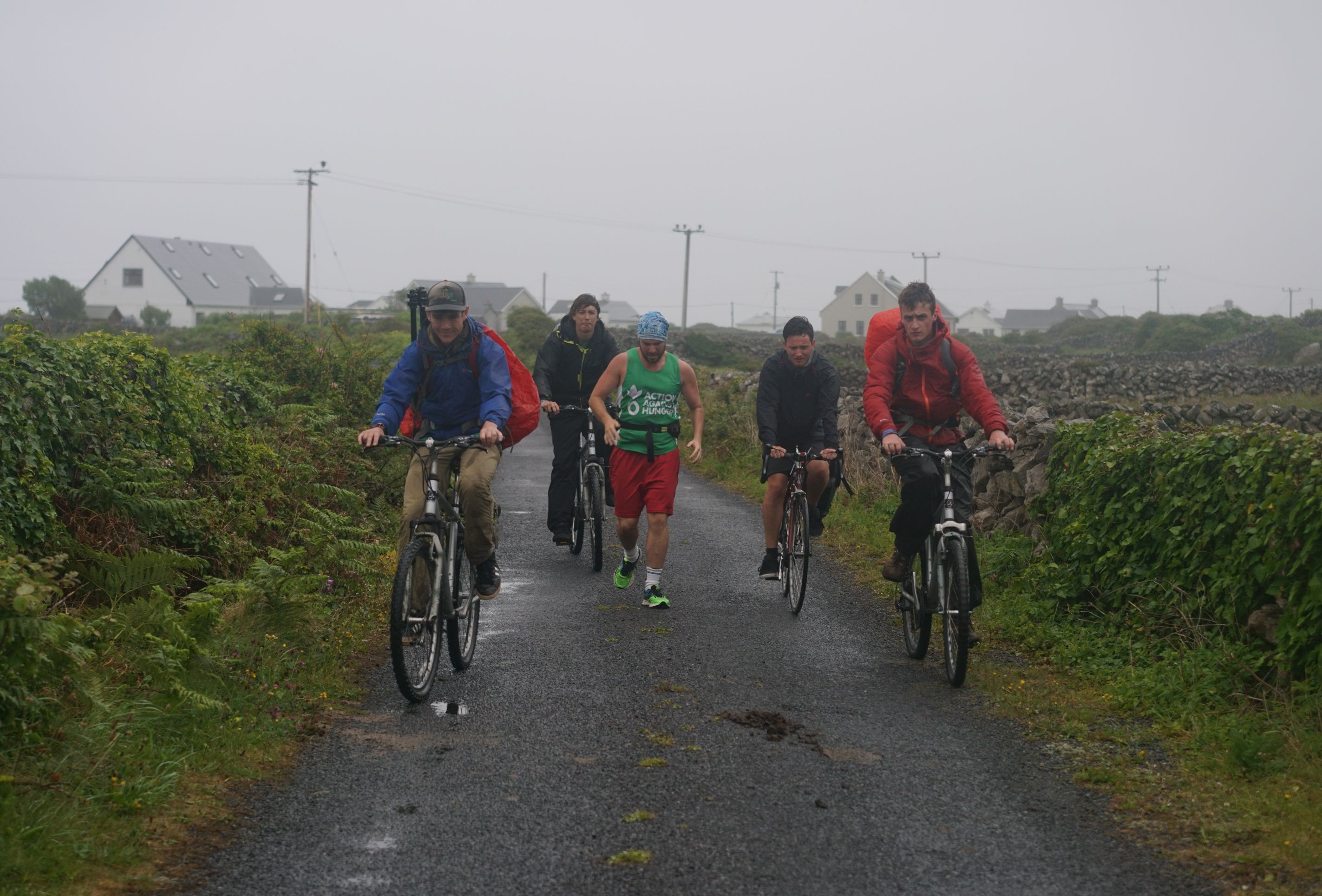 The crew of Dave Goes West rides bikes alongside Dave in the rain.