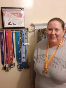 A woman standing next to medals she received for running races.