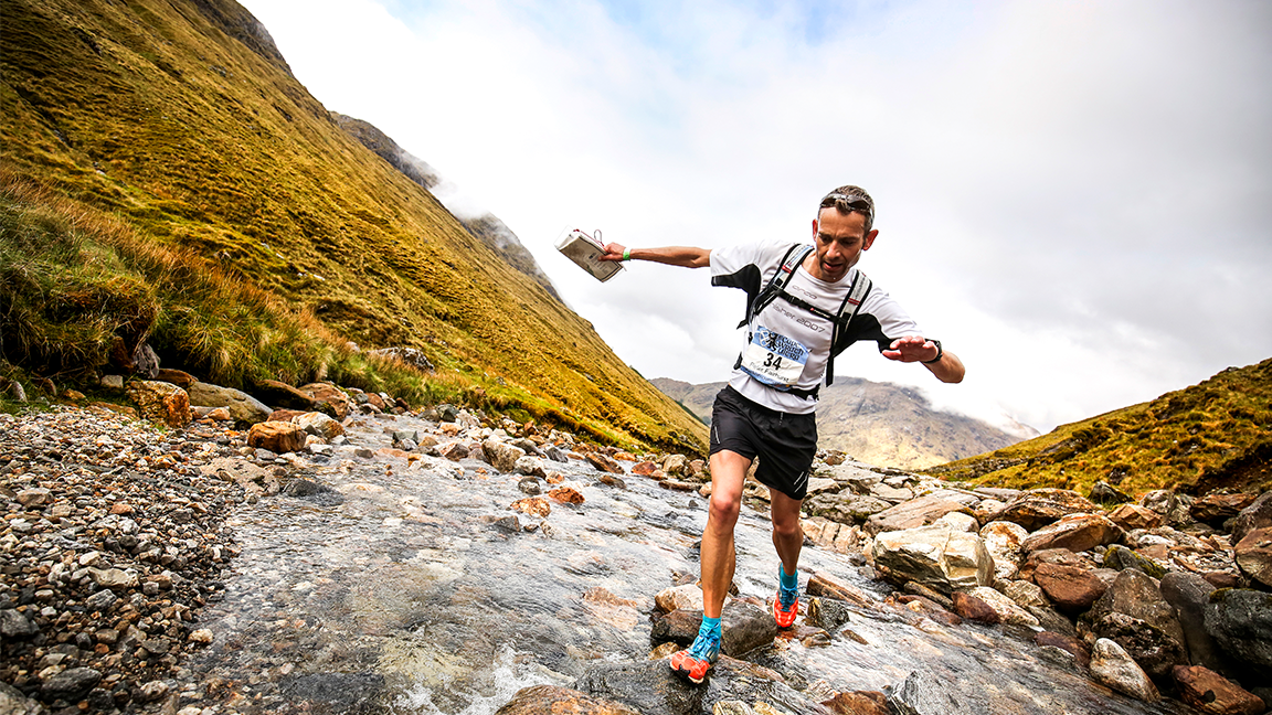 man runs over rocks and stream in race