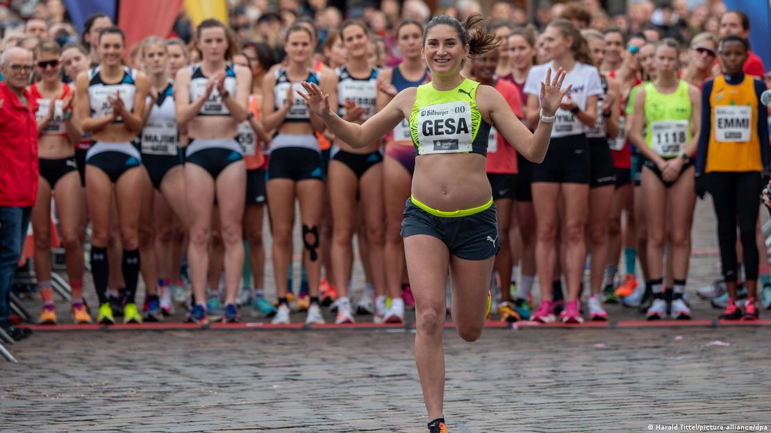 Runner Gesa Krause waves her hands while running with fellow runners applauding behind her