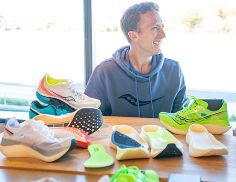 a man sitting next to saucony shoe prototypes laid out on a desk