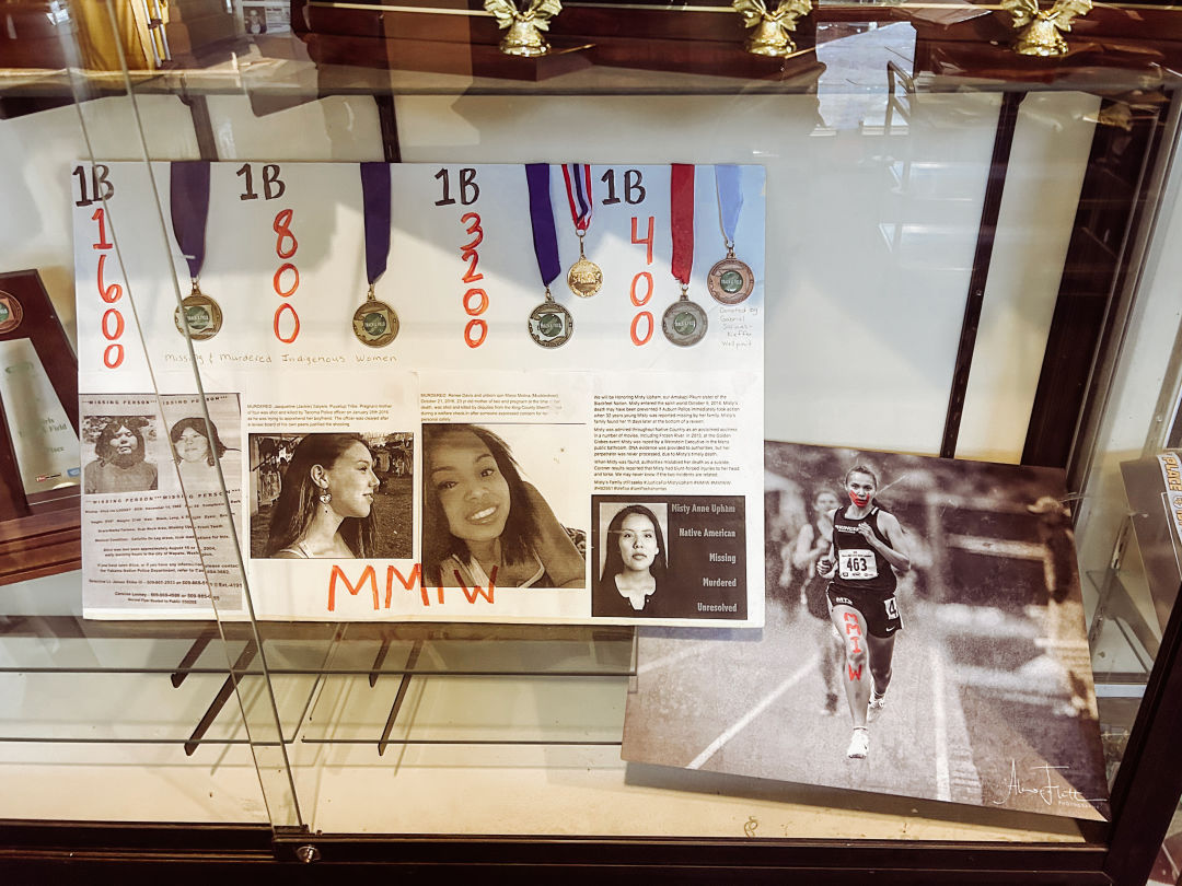 The poster of missing and murdered Indigenous women and viral image of Rosalie Fish running at the 2019 state meet sit in a trophy case outside the Muckleshoot Tribal School gym.