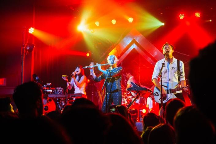 a band plays on stage with a woman in front playing the flute. Red and yellow and green lights.