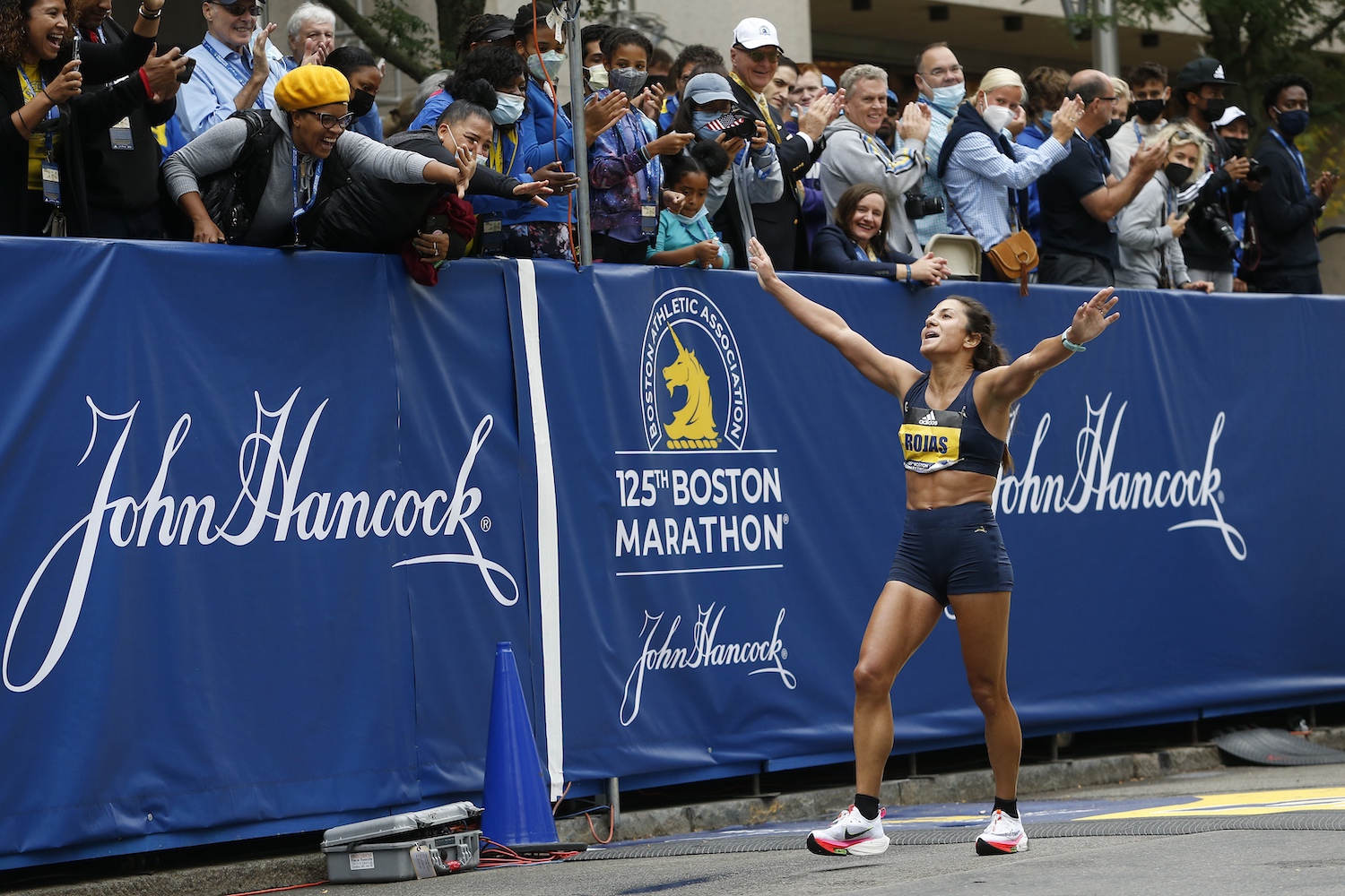 A top finisher at the Boston Marathon is cheered by fans in the stands behind her.